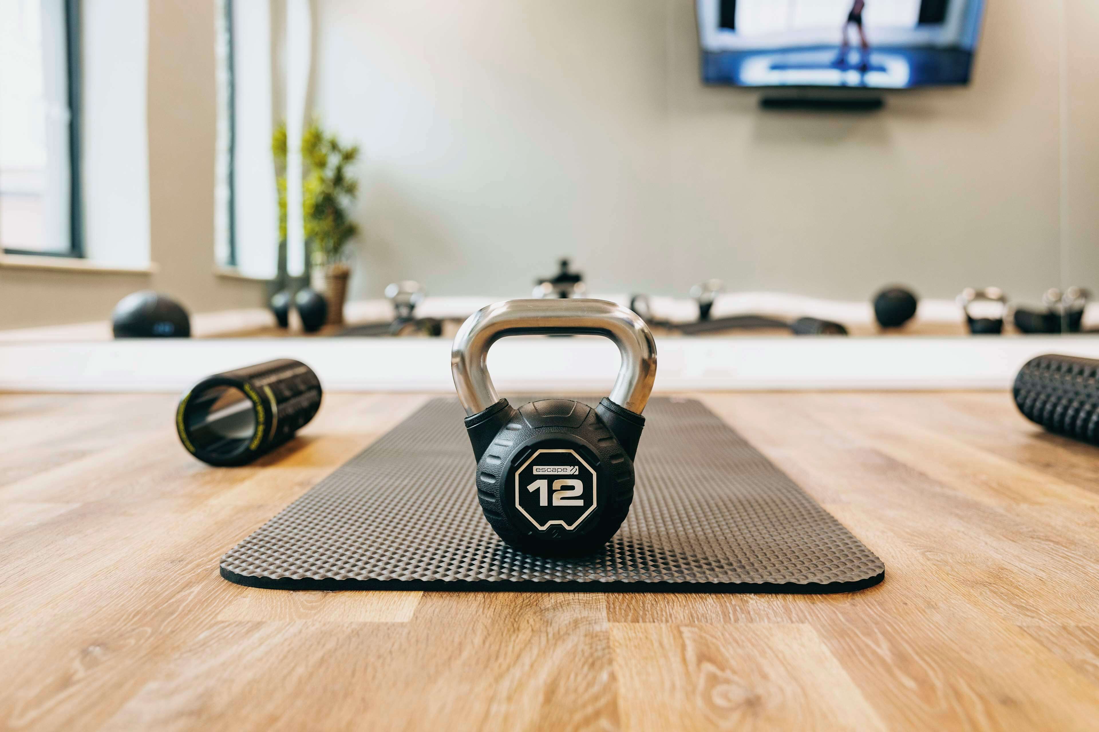 Un kettlebell su un tappetino, con un pavimento in legno e una TV sullo sfondo.