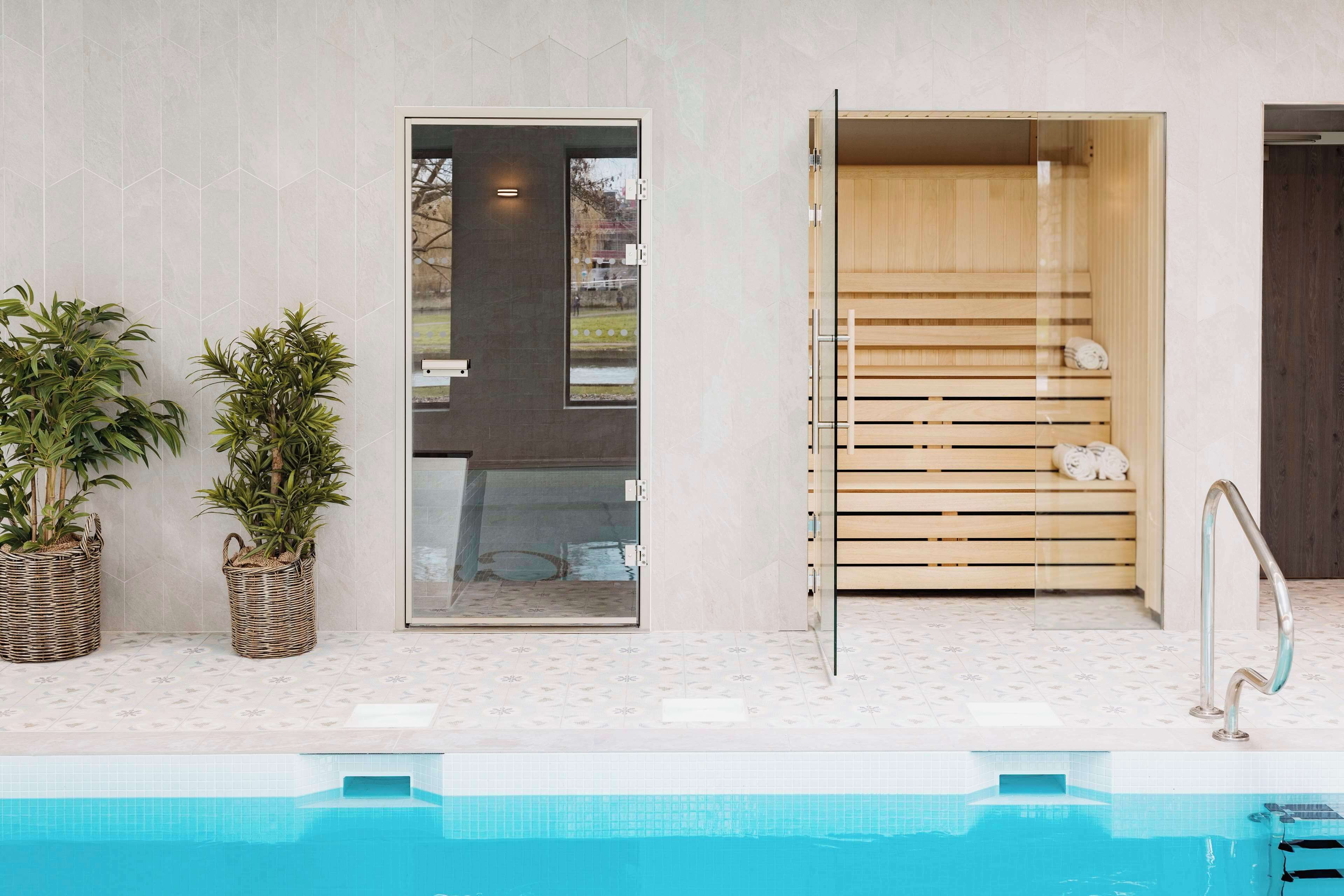 A modern spa area with a glass door leading to a sauna, a wooden bench, and a poolside area with potted plants.