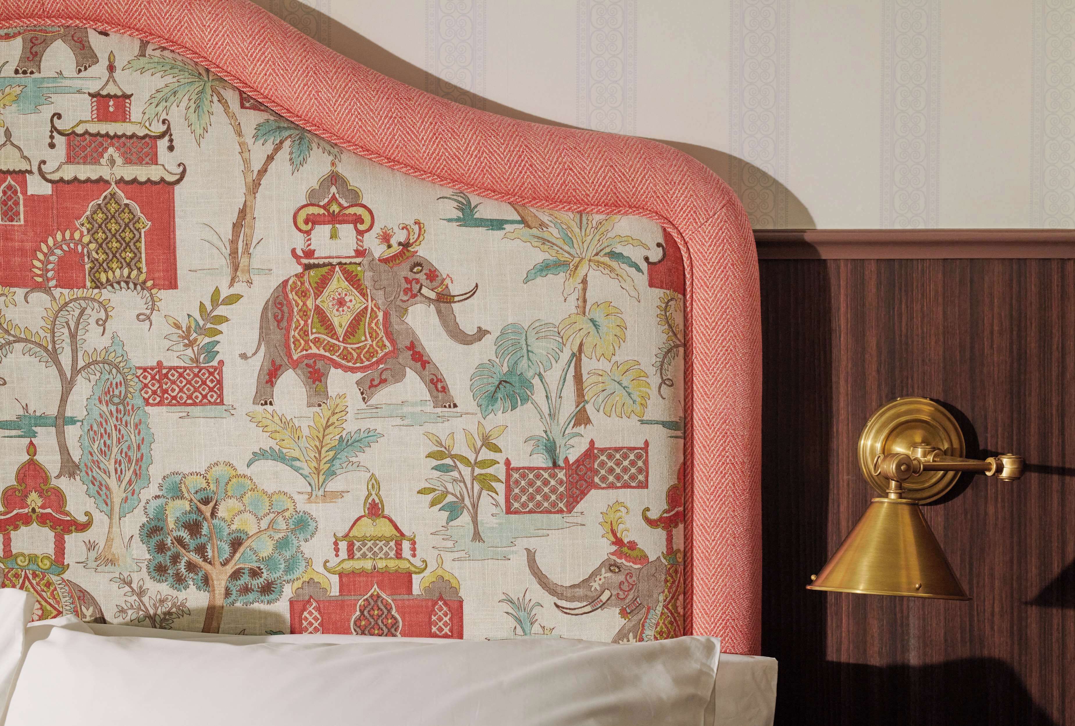 A bed with a headboard featuring a traditional design with elephants and buildings, a brass door handle, and a patterned wall in the background.