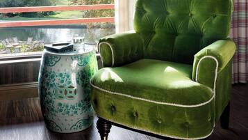 A green upholstered armchair with a tufted backrest and button details, positioned next to a decorative ceramic vase with a floral pattern.