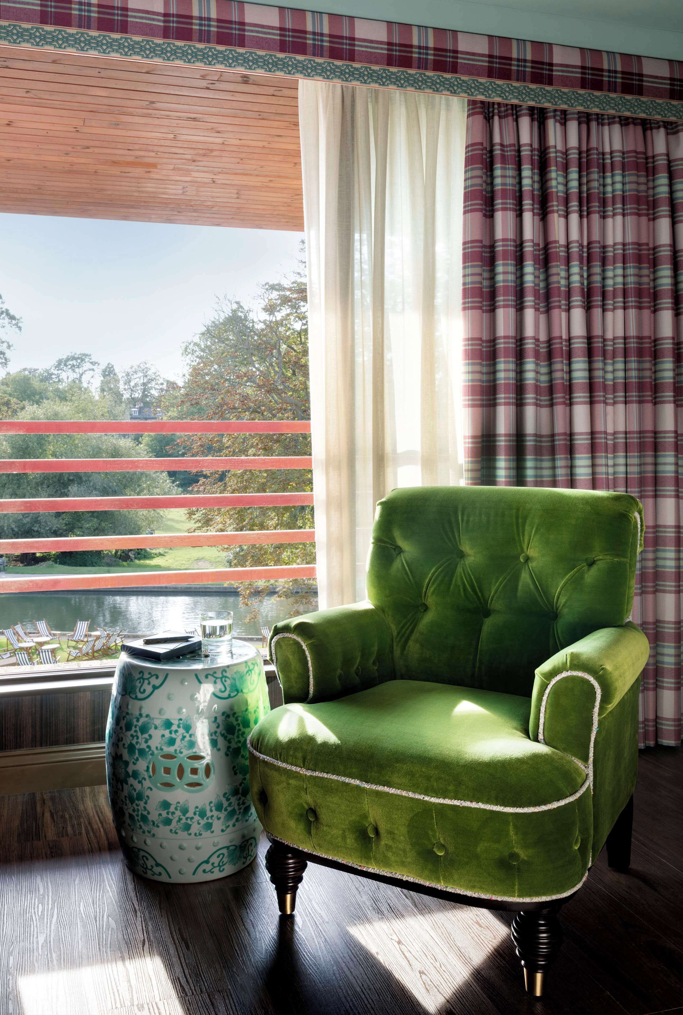A green armchair by a window with a view of a lake and trees.