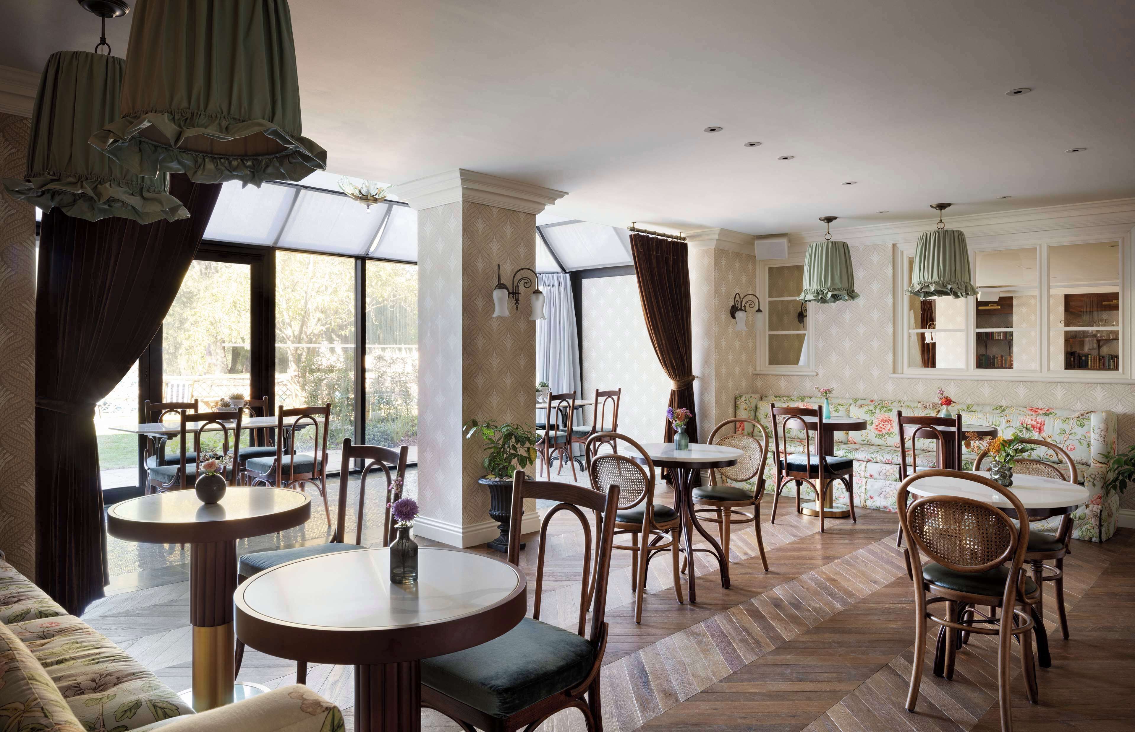 A dining area with round tables and chairs, large windows, and hanging green lamps.