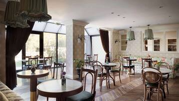 A dining area with round tables and chairs, large windows, and hanging green lamps.