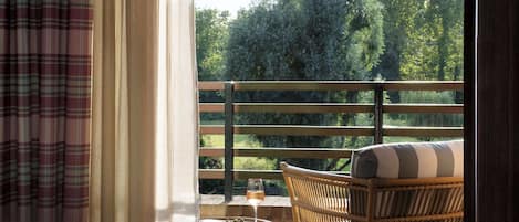 Una habitación con una cama, un sillón de mimbre, una mesita y vistas al exterior.