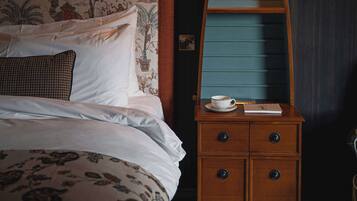 A neatly made bed with a patterned headboard, a bedside table with a cup and a book, and a blue wall with a decorative panel.