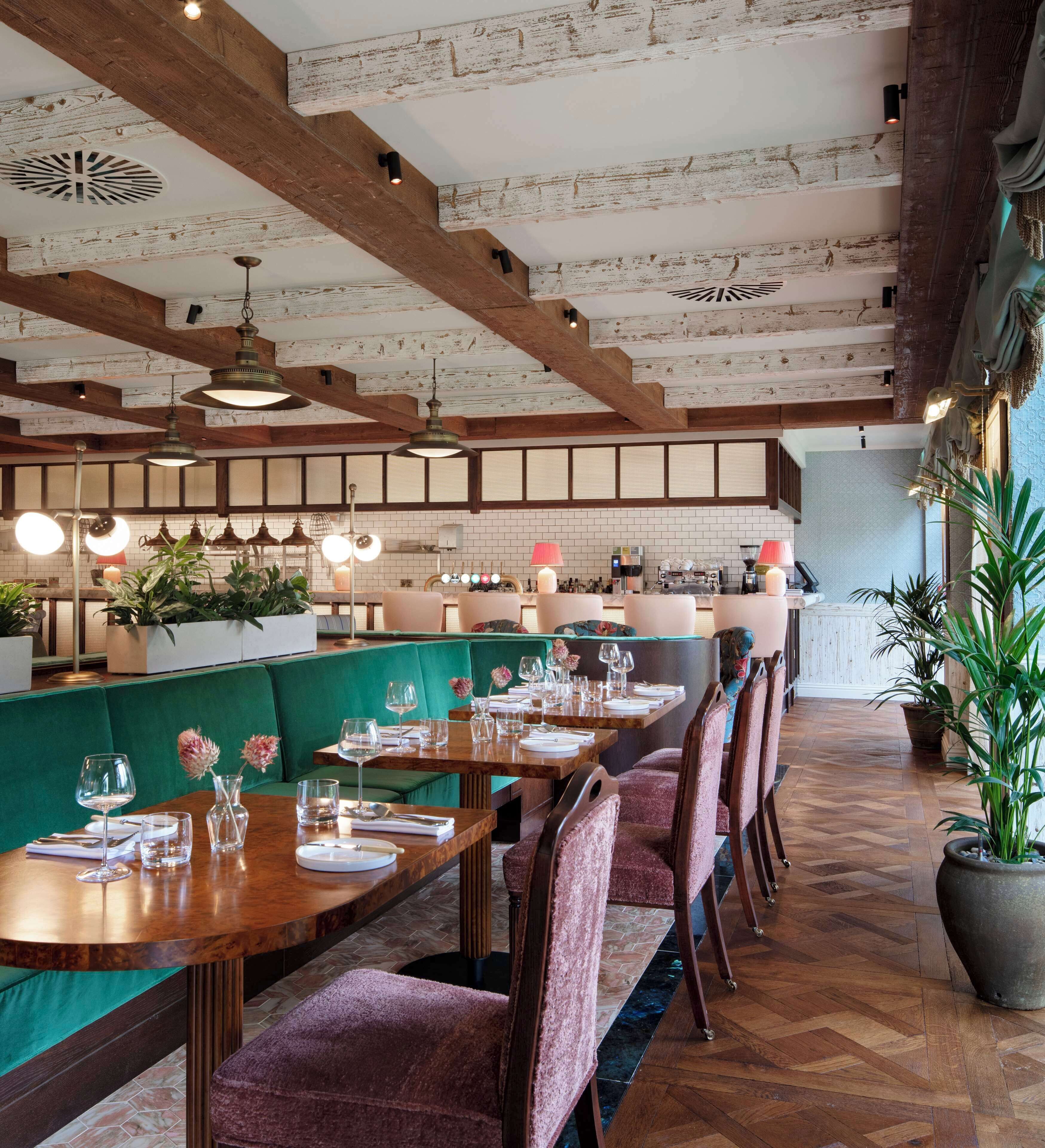 A restaurant with wooden beams, green upholstered booths, and a long wooden bar.