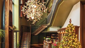 A spacious interior with a grand staircase, a wooden floor, a green sofa, a Christmas tree, and a chandelier. - Graduate by Hilton Cambridge (Cambridge)