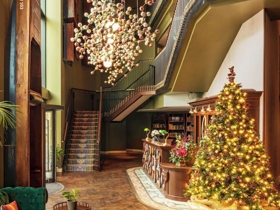 Ein großzügiger Innenraum mit einer imposanten Treppe, Holzboden, einem grünen Sofa, einem Weihnachtsbaum und einer Chandelier.