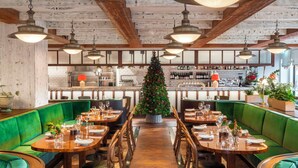A restaurant with green upholstered booths, wooden tables, and hanging pendant lights. A Christmas tree is in the center.