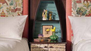 Quarto com cama, mesa de cabeceira, prateleira com objetos decorativos e parede com papel de parede estampado.