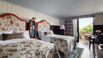 Habitación de hotel con dos camas, un escritorio, una silla, una estantería y vistas al exterior.