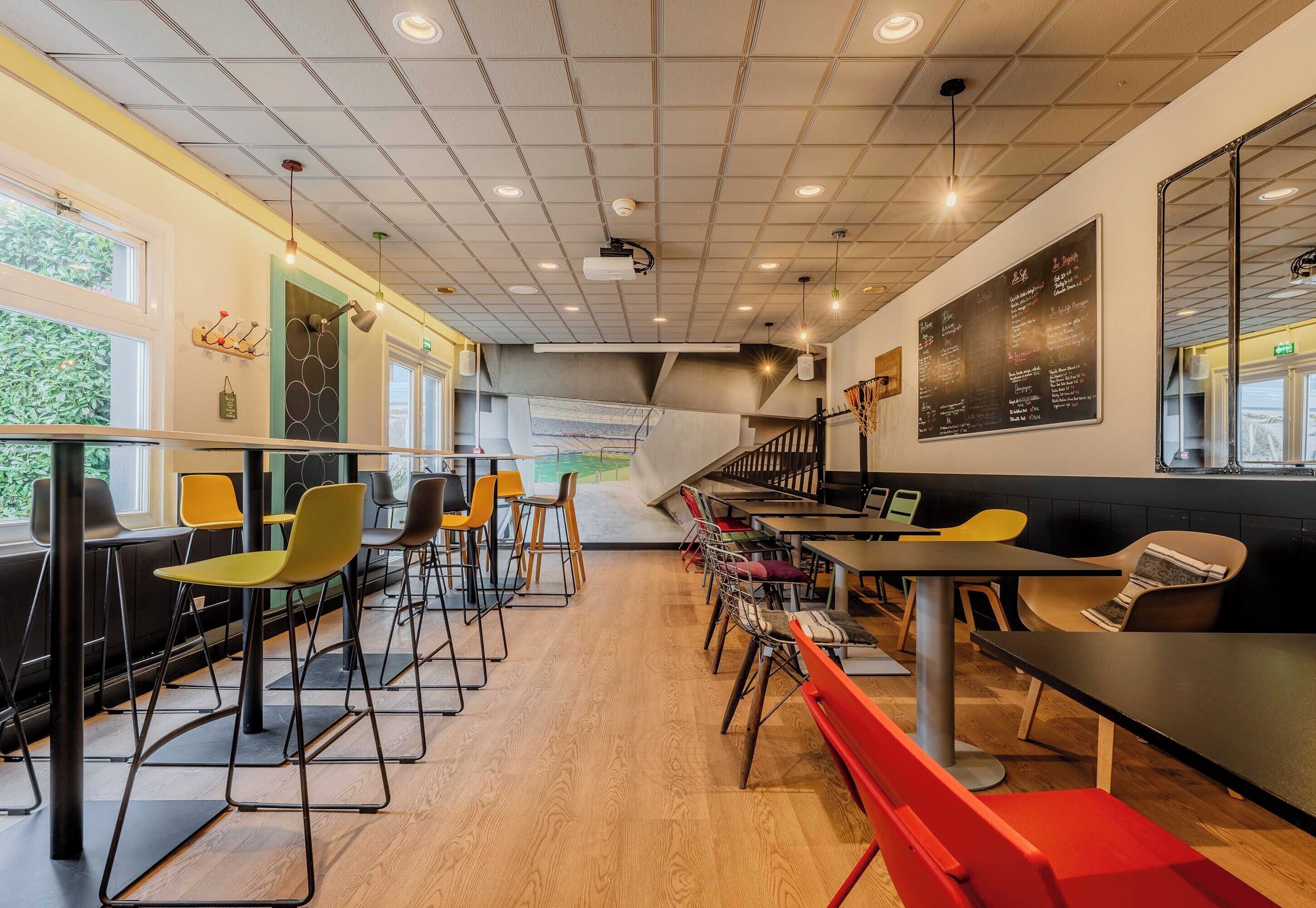 Una cafetería moderna con suelo de madera, sillas negras y amarillas, y un menú en una pizarra en la pared.
