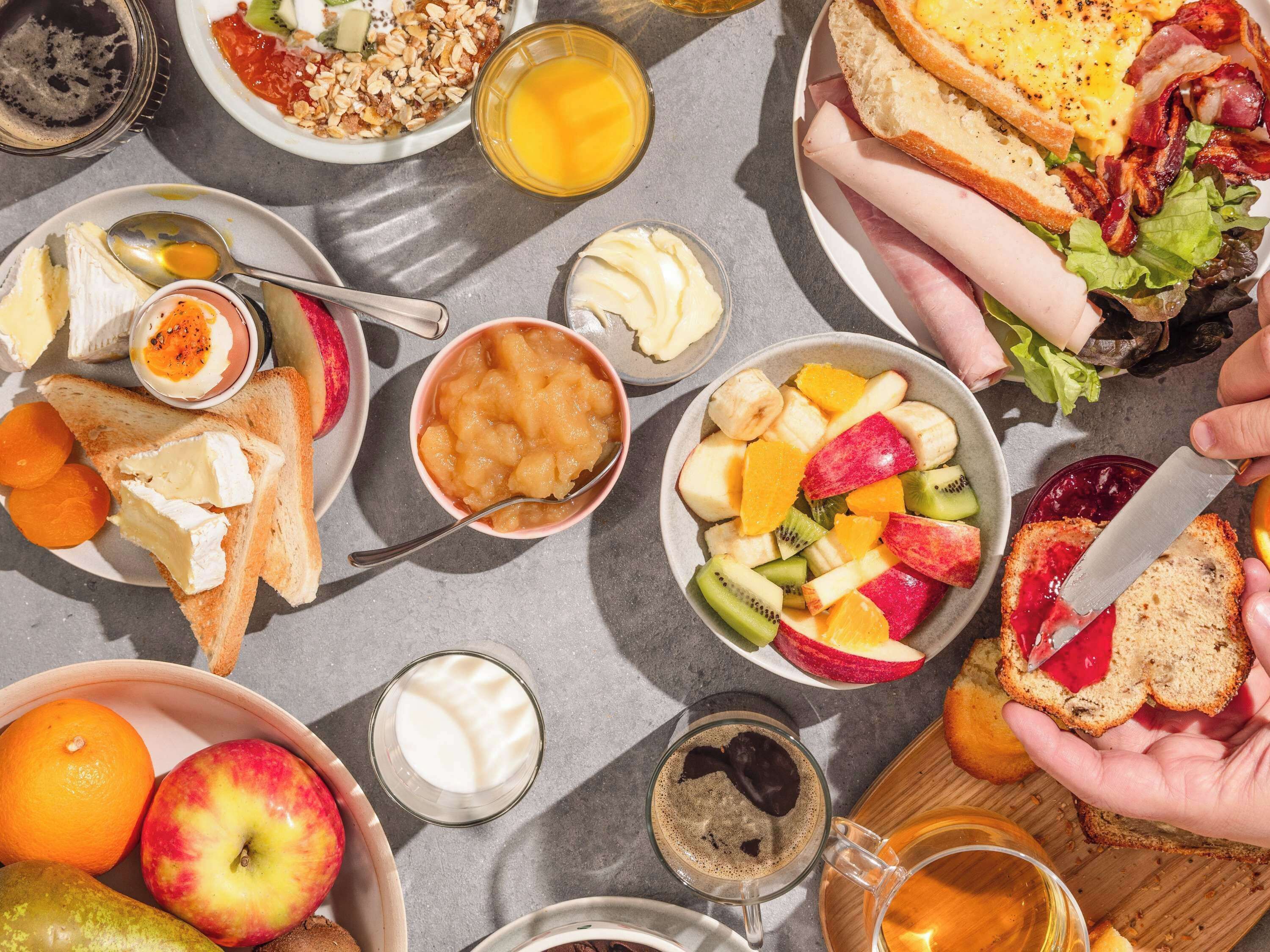 Una mesa de desayuno con diversos alimentos, como tostadas, fruta, huevos y bebidas.