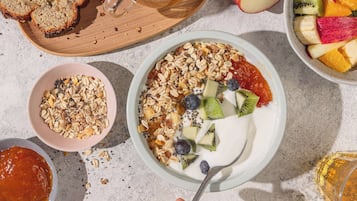Une table mise pour le petit-déjeuner, avec un bol de yaourt garni de granola, de fruits et une cuillère.
