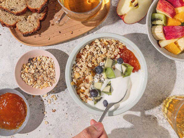 Un desayuno con un tazón de yogur cubierto de granola, frutas y una cuchara.