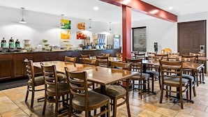 Un restaurant avec des tables et des chaises en bois, un comptoir où sont exposés divers produits alimentaires, et un mur où sont présentés des fruits et des boissons.