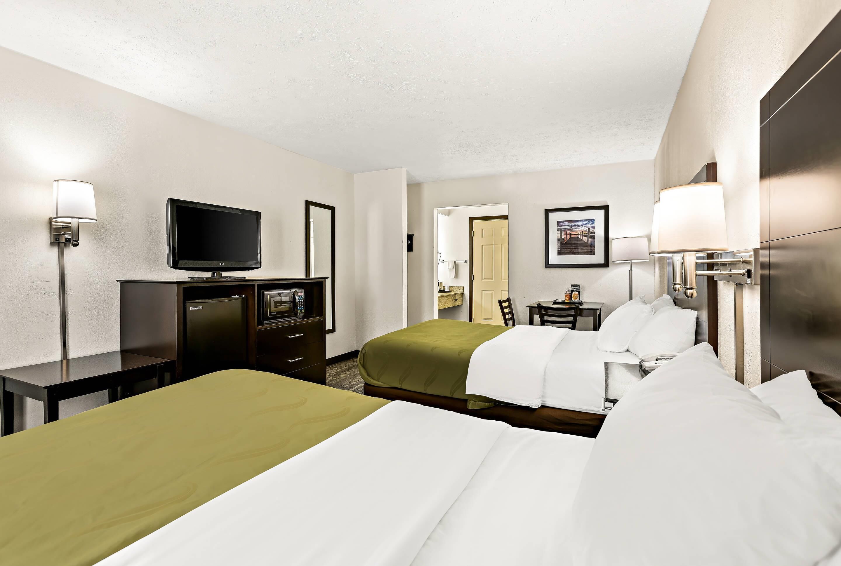 A hotel room with two beds, a television, a desk, and a chair.