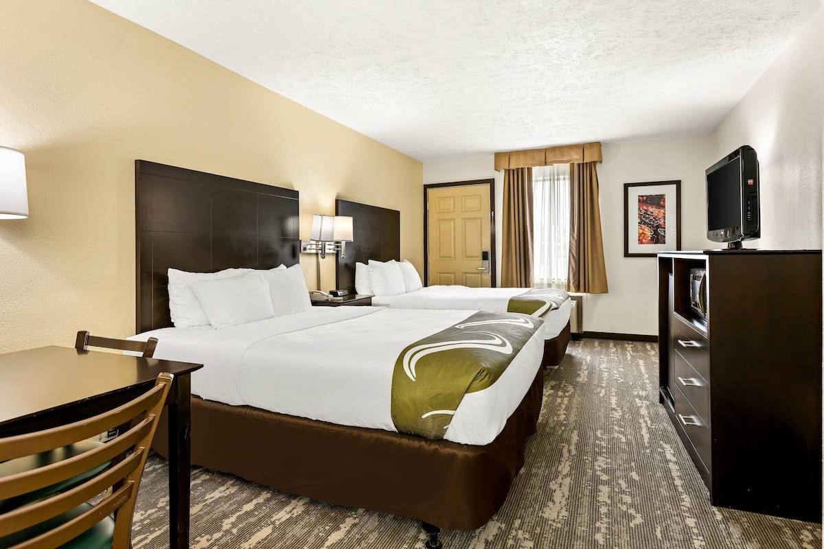 A hotel room with two beds, a desk, a chair, a television, and a door.