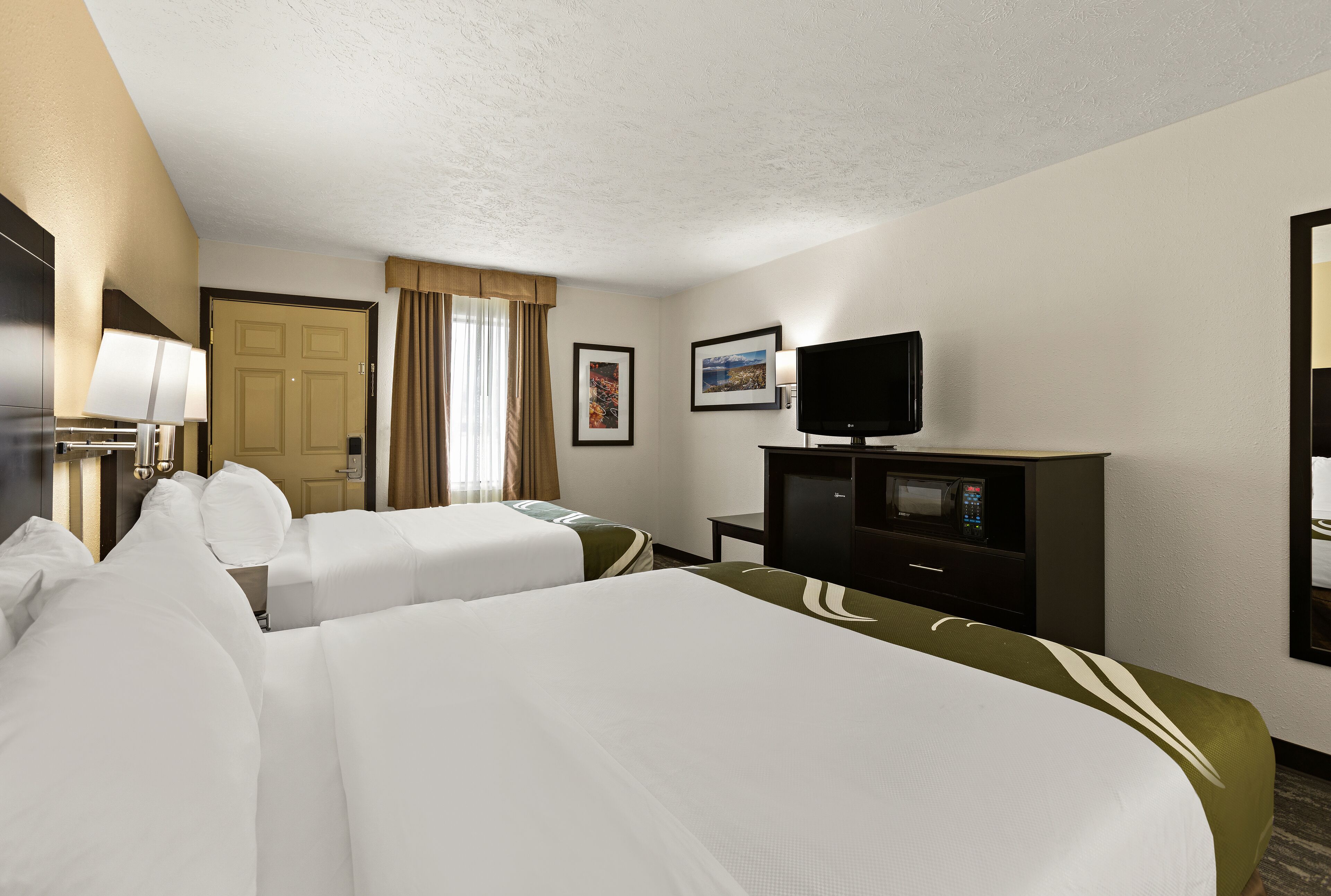 A hotel room with two beds, a television, a desk, and a door.