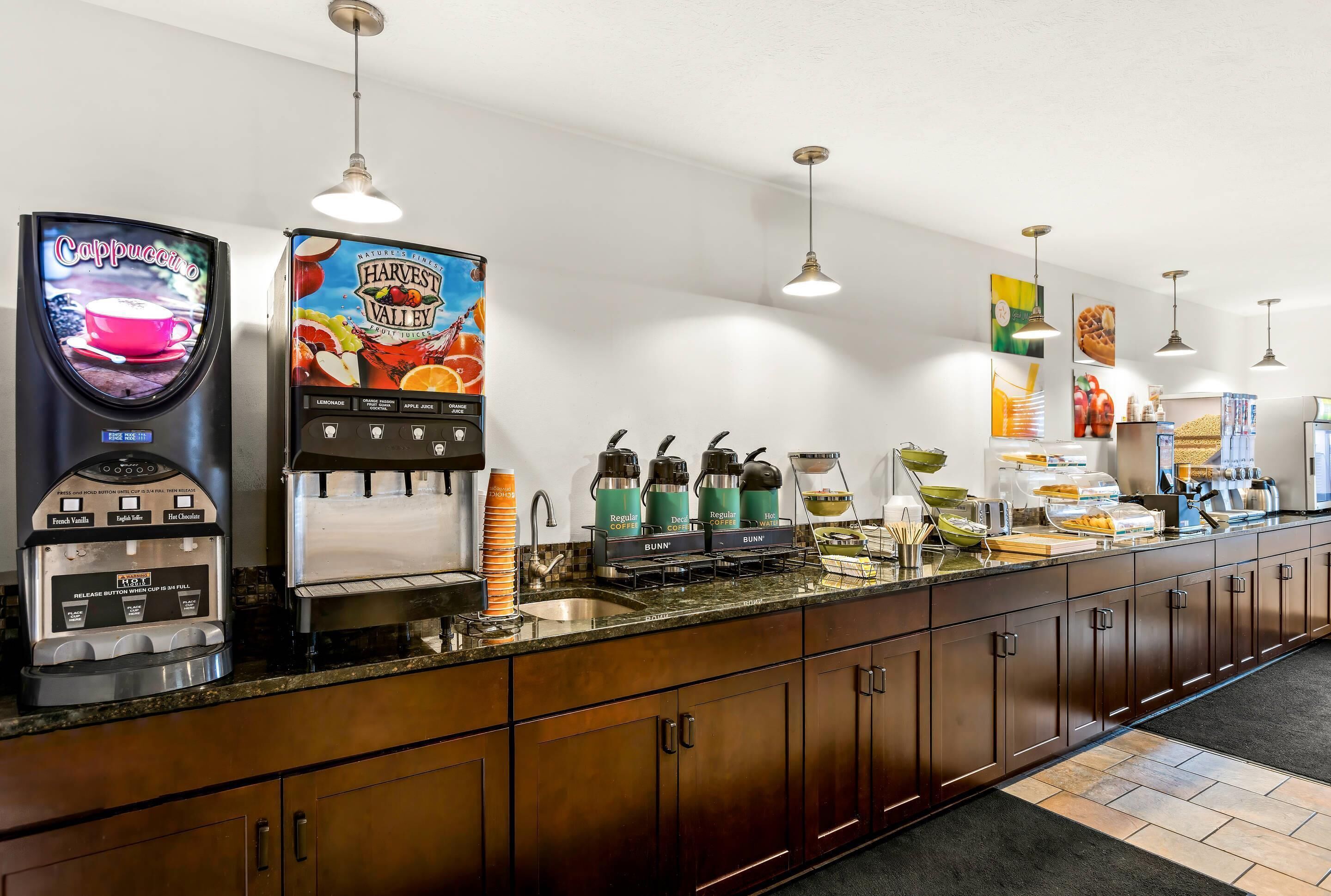 A hotel breakfast area with a coffee machine, a juice dispenser, and a beverage cooler.