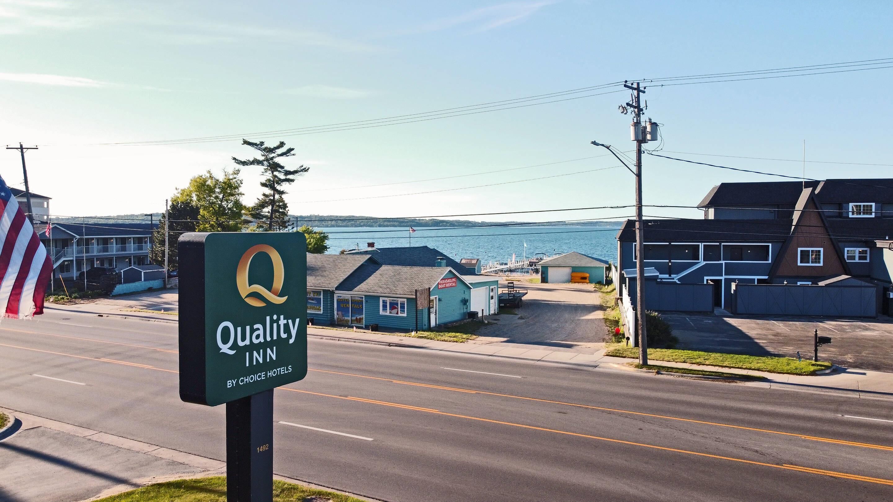 A Quality Inn sign by Choice Hotels with a view of a waterfront and residential buildings.