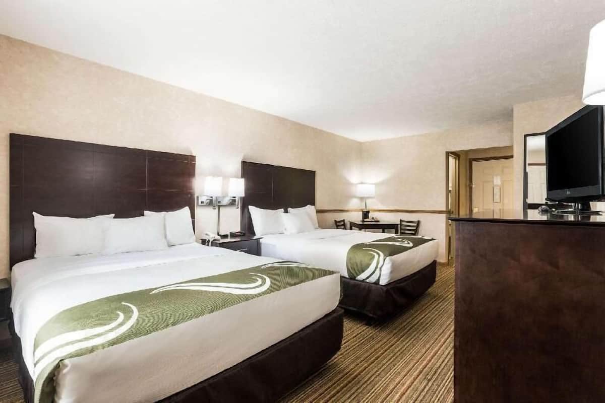 A hotel room with two beds, a desk, a television, and a lamp.
