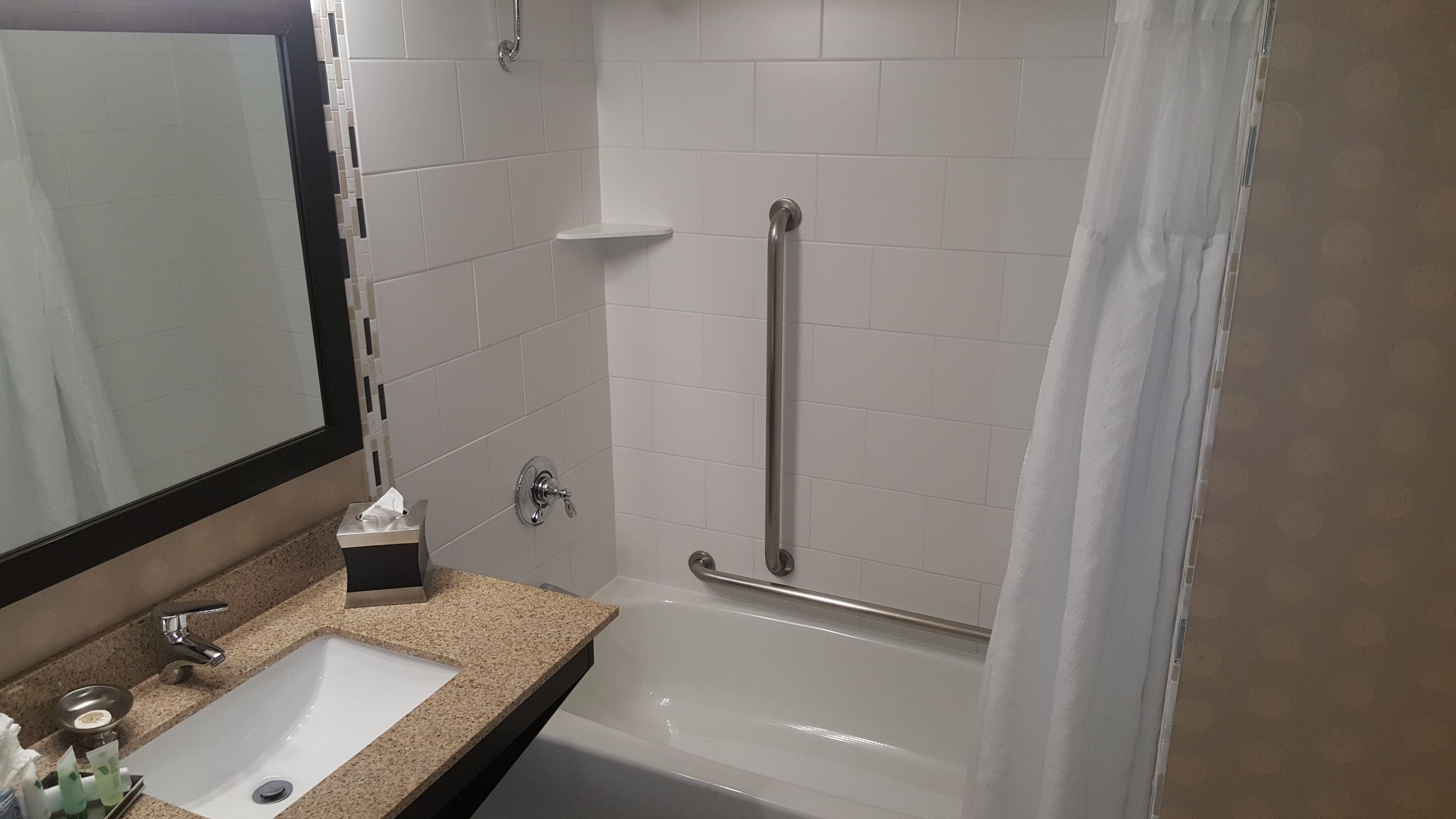 A bathroom with a white sink, a mirror, a towel rack, and a shower with a grab bar.