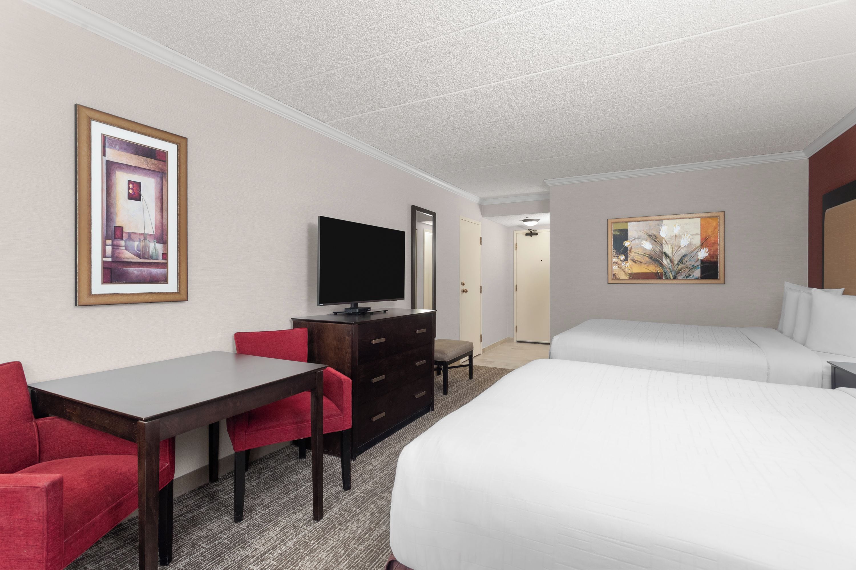 A hotel room with a bed, a desk, a chair, a television, and a painting on the wall.