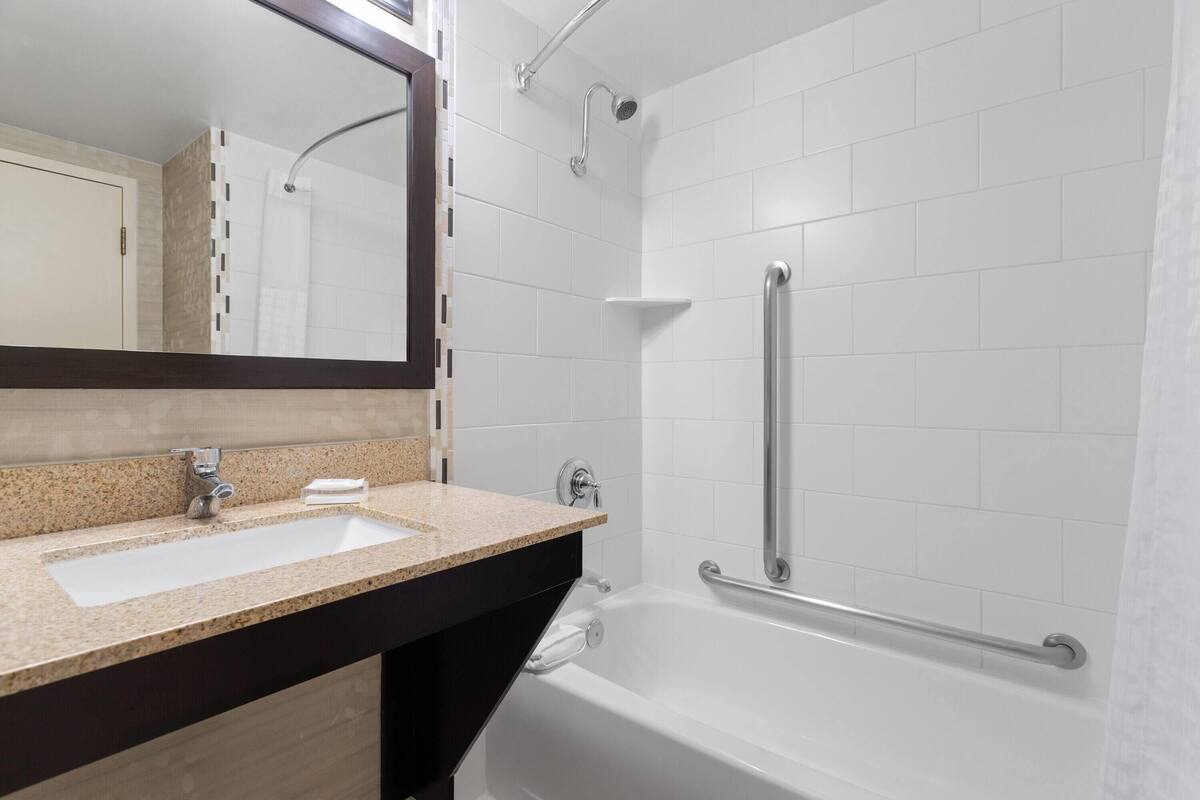A bathroom with a white sink, a mirror, a shower with a grab bar, and a bathtub.
