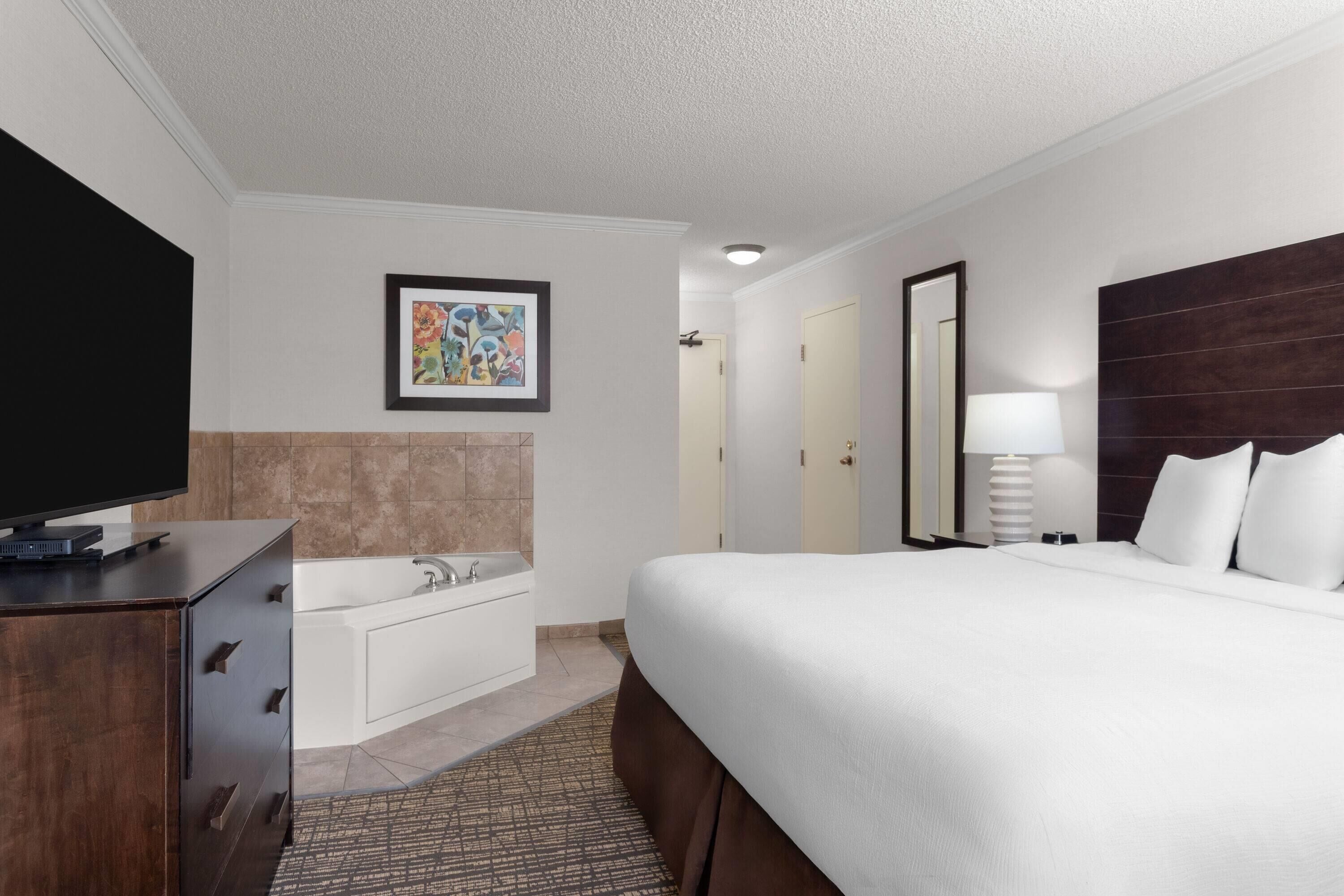 Une chambre d’hôtel avec un grand lit, une télévision à écran plat, une baignoire et une œuvre d’art encadrée au mur.
