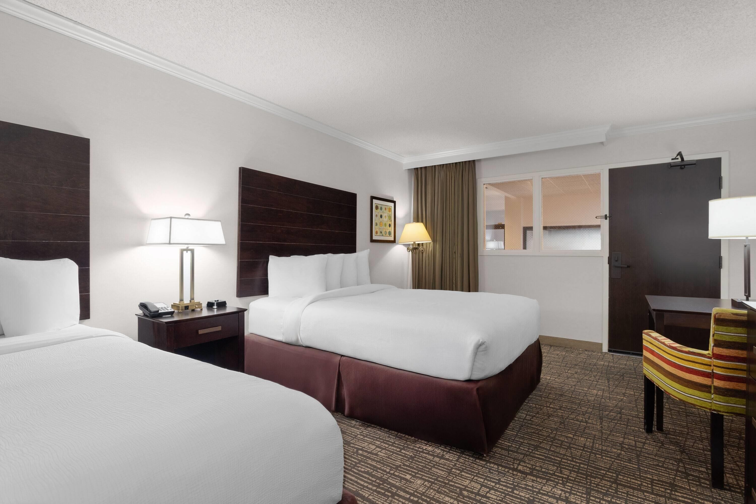 A hotel room with two beds, a desk, a chair, and a door.