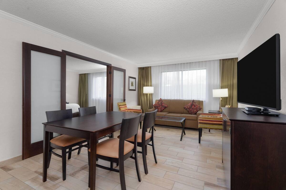 A hotel room with a dining table, chairs, a sofa, a TV, and a desk.