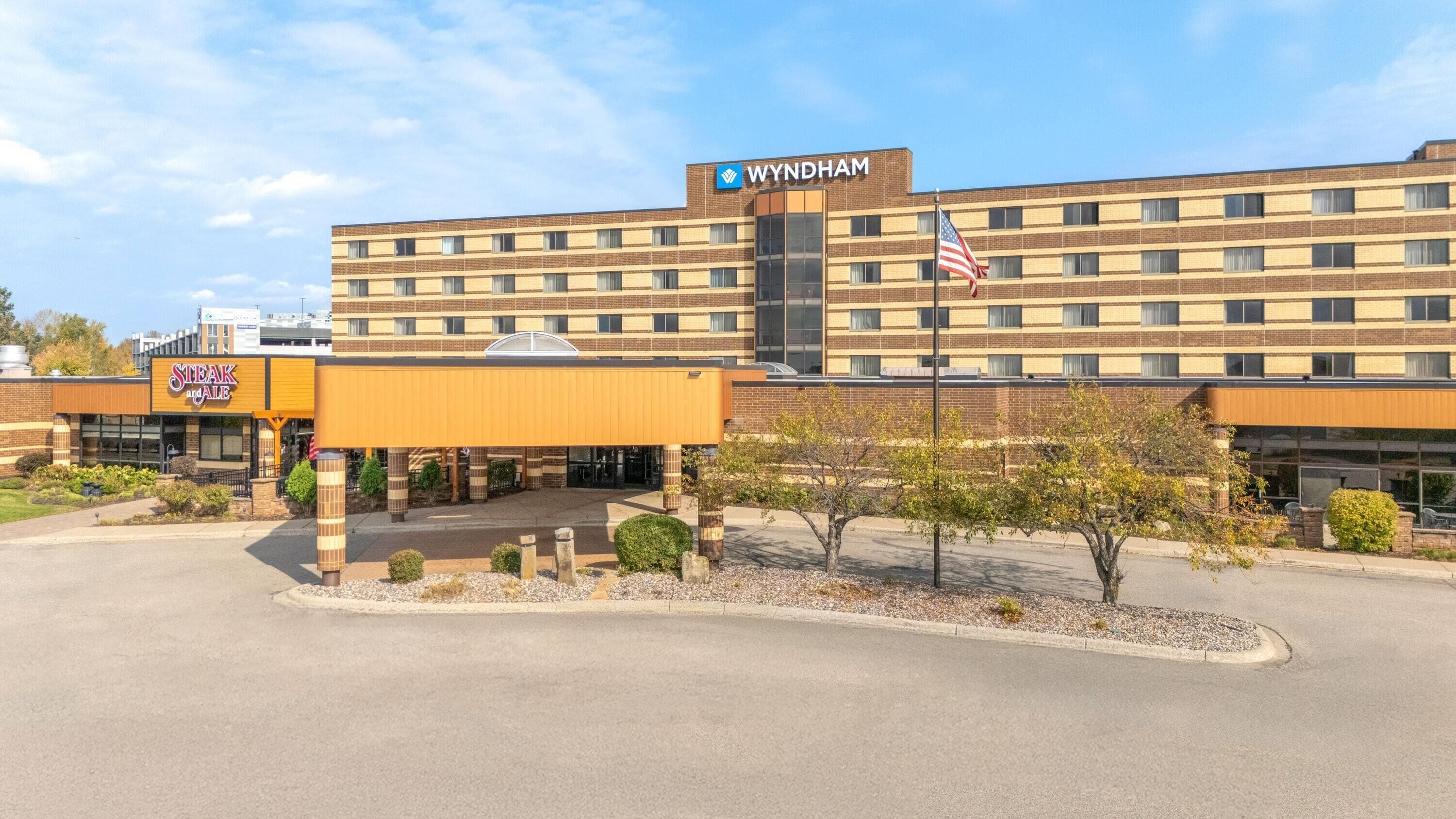Um hotel Wyndham com fachada de tijolos, entrada coberta e placa do restaurante Steak and Ale.
