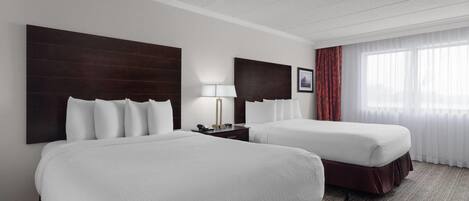 A hotel room with two beds, a nightstand with a lamp, and a large window with curtains.