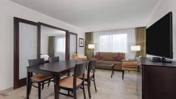A hotel room with a dining table, chairs, a sofa, a television, and a bed.