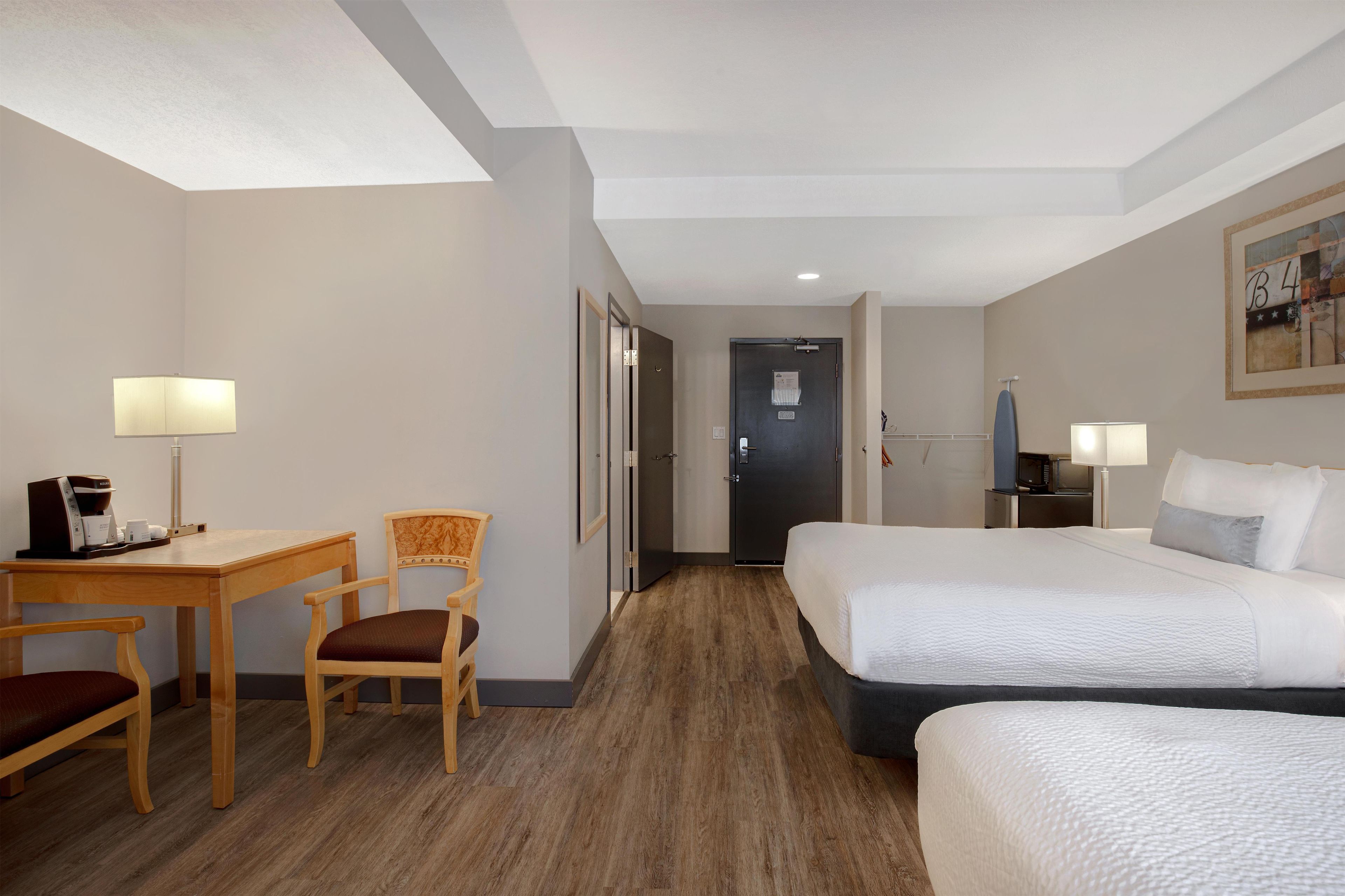 A hotel room with a bed, a desk, a chair, a microwave, and a door.