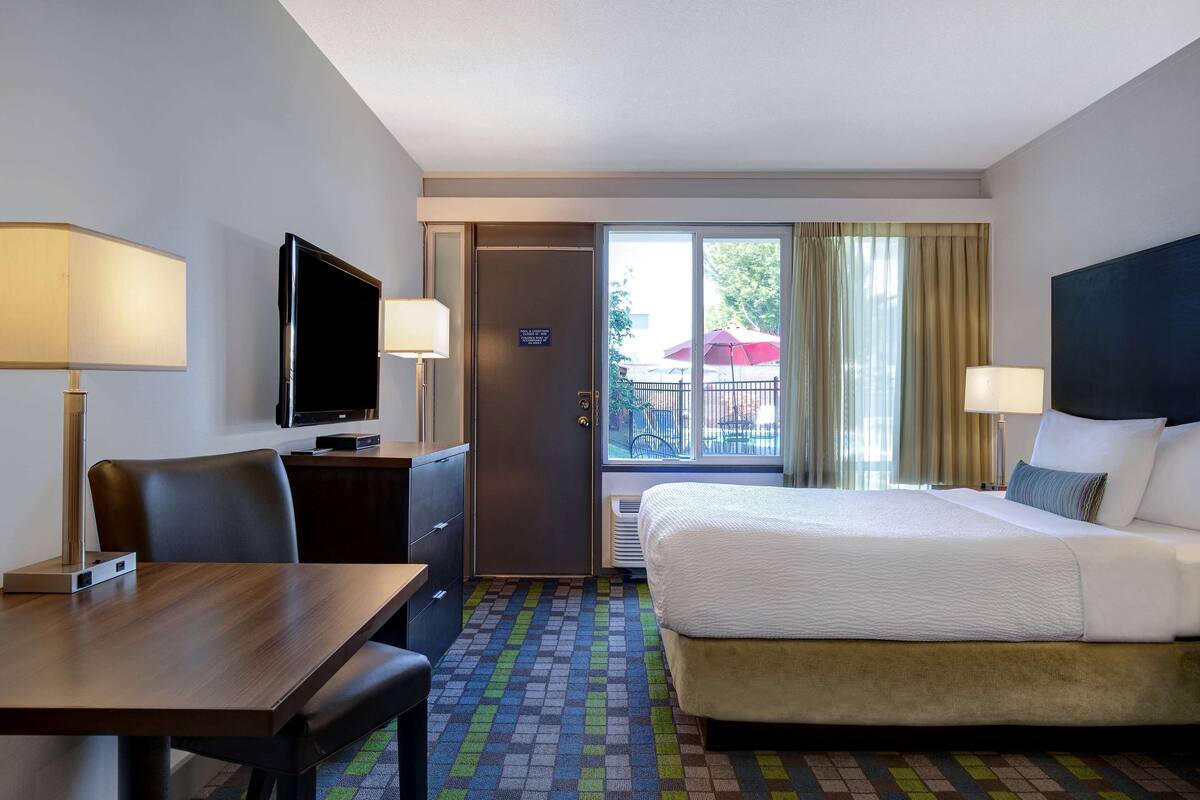 Ein Hotelzimmer mit Bett, Schreibtisch, Fernseher und einem Fenster mit Vorhängen.