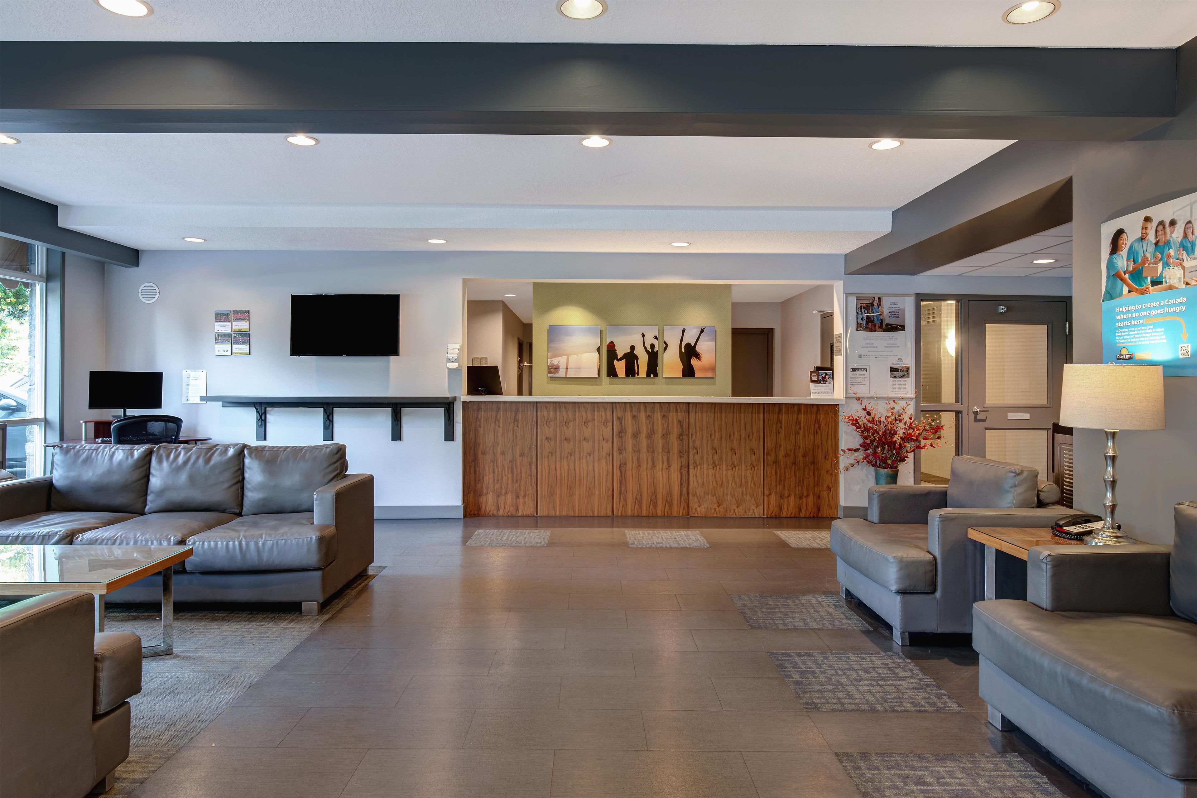 A modern hotel lobby with a reception desk, seating area, and a flat-screen TV mounted on the wall.