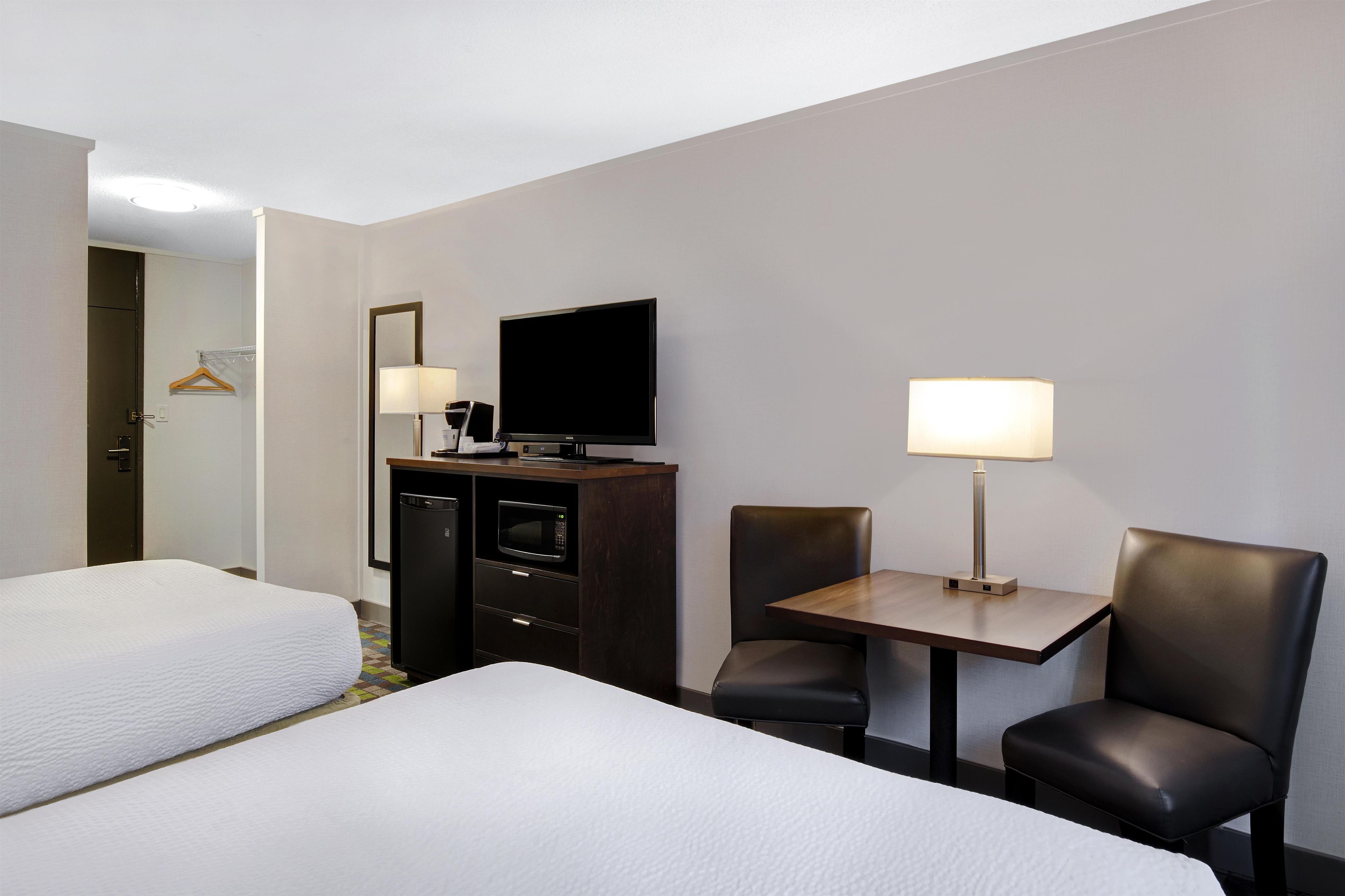 Une chambre d’hôtel avec deux lits, un bureau avec une chaise, une télévision et un mini-bar.