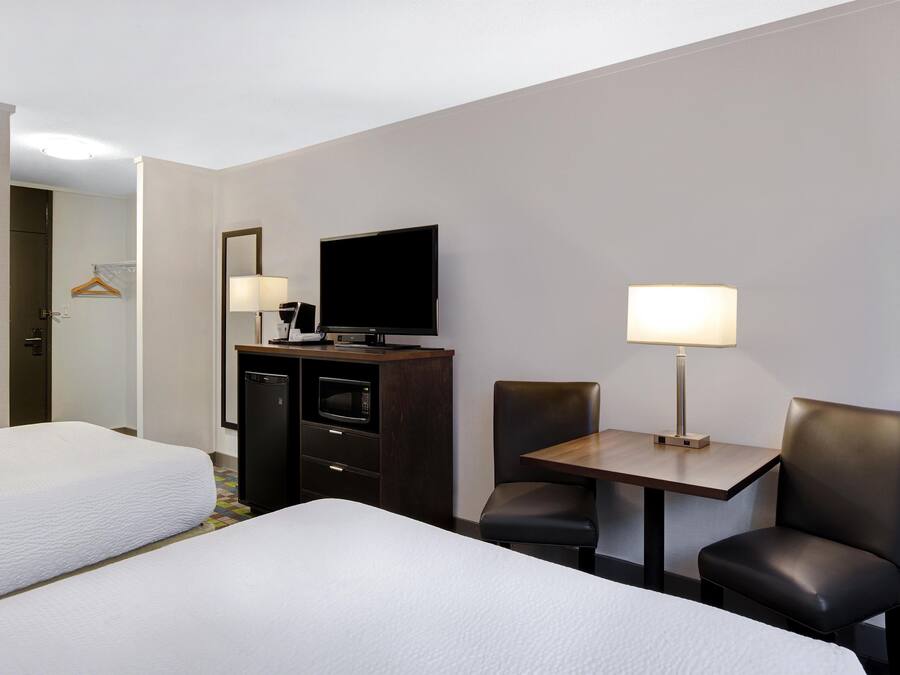 Une chambre d’hôtel avec deux lits, un bureau avec une chaise, une télévision et un mini-bar.