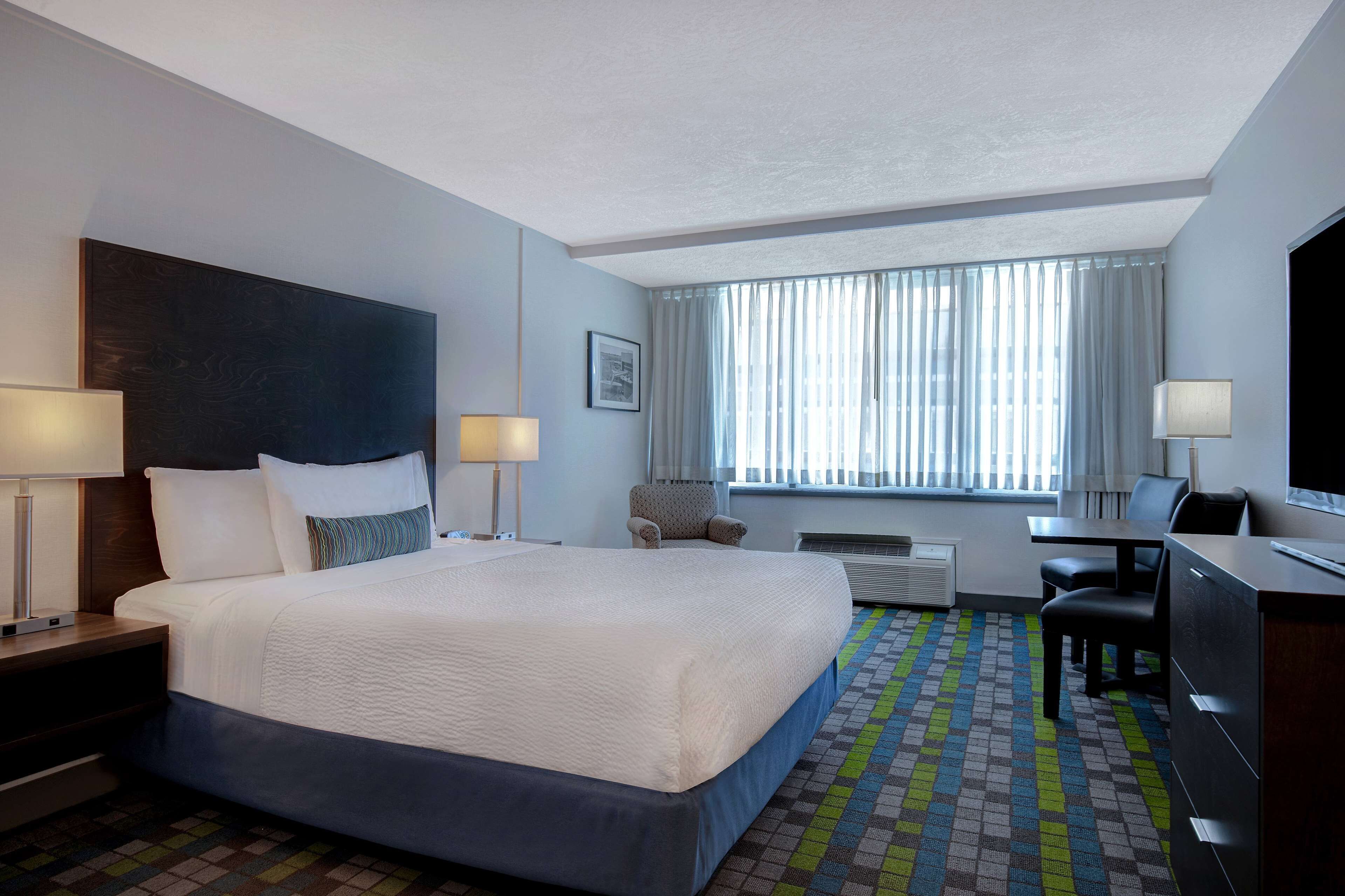 A hotel room with a large bed, two bedside tables, a desk, a chair, and a television.