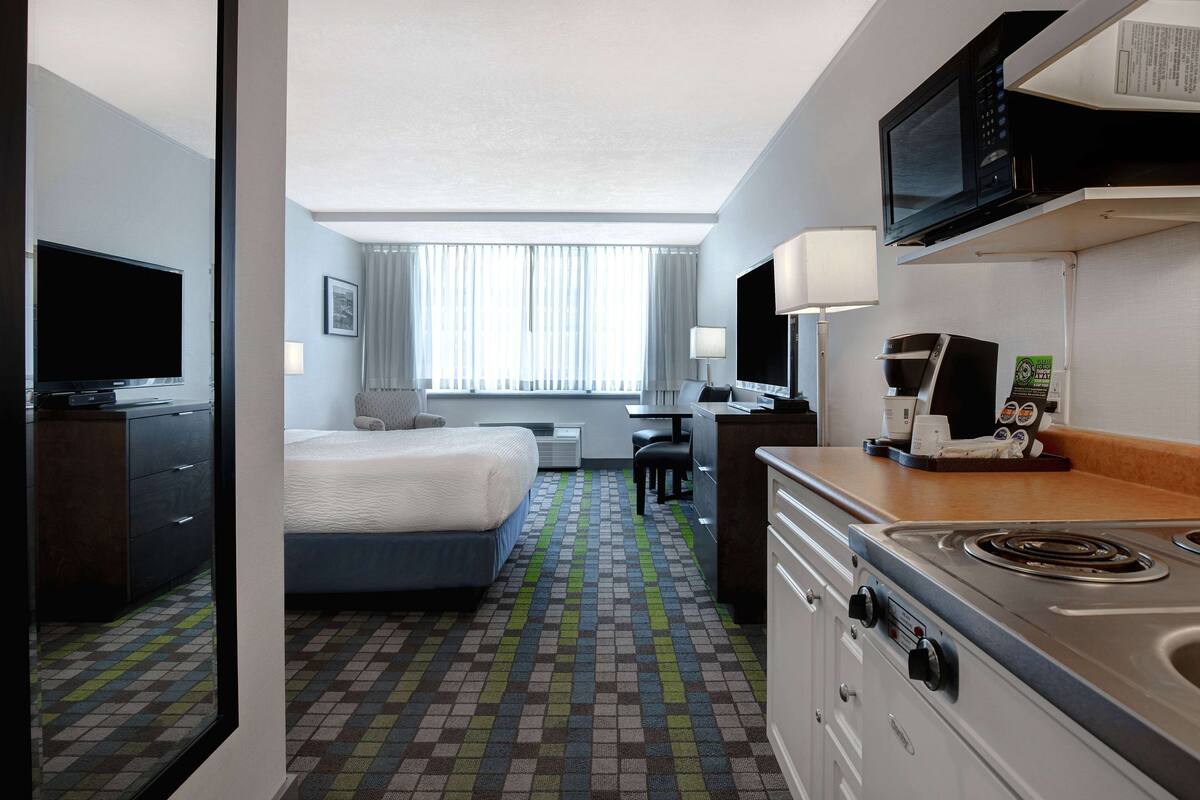 Ein Hotelzimmer mit Bett, Schreibtisch, Mikrowelle, Herd und Fernseher.