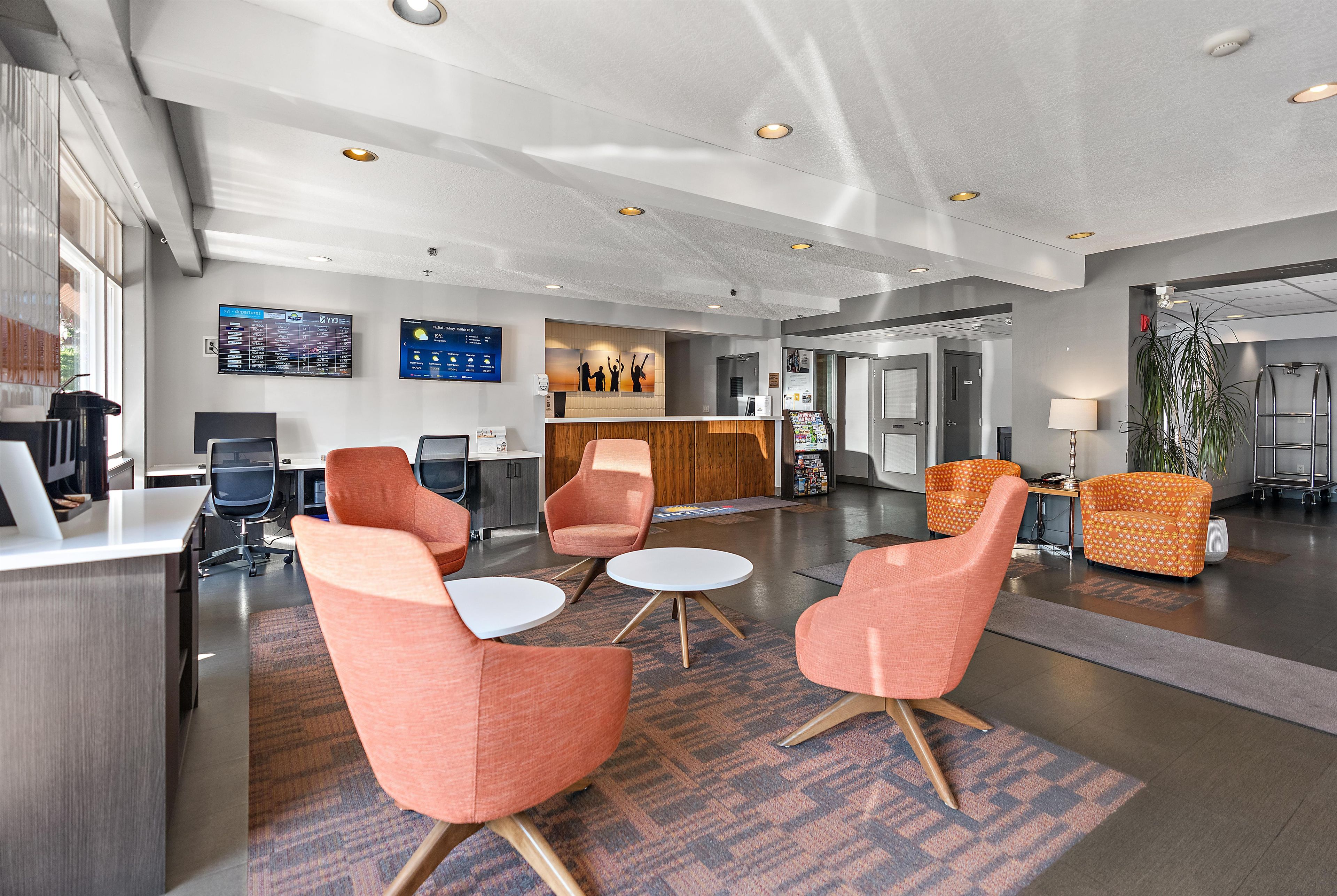 Un hall d’hôtel moderne, doté d’espaces aménagés avec des sièges, d’un comptoir d’accueil et d’un panneau d’affichage numérique.