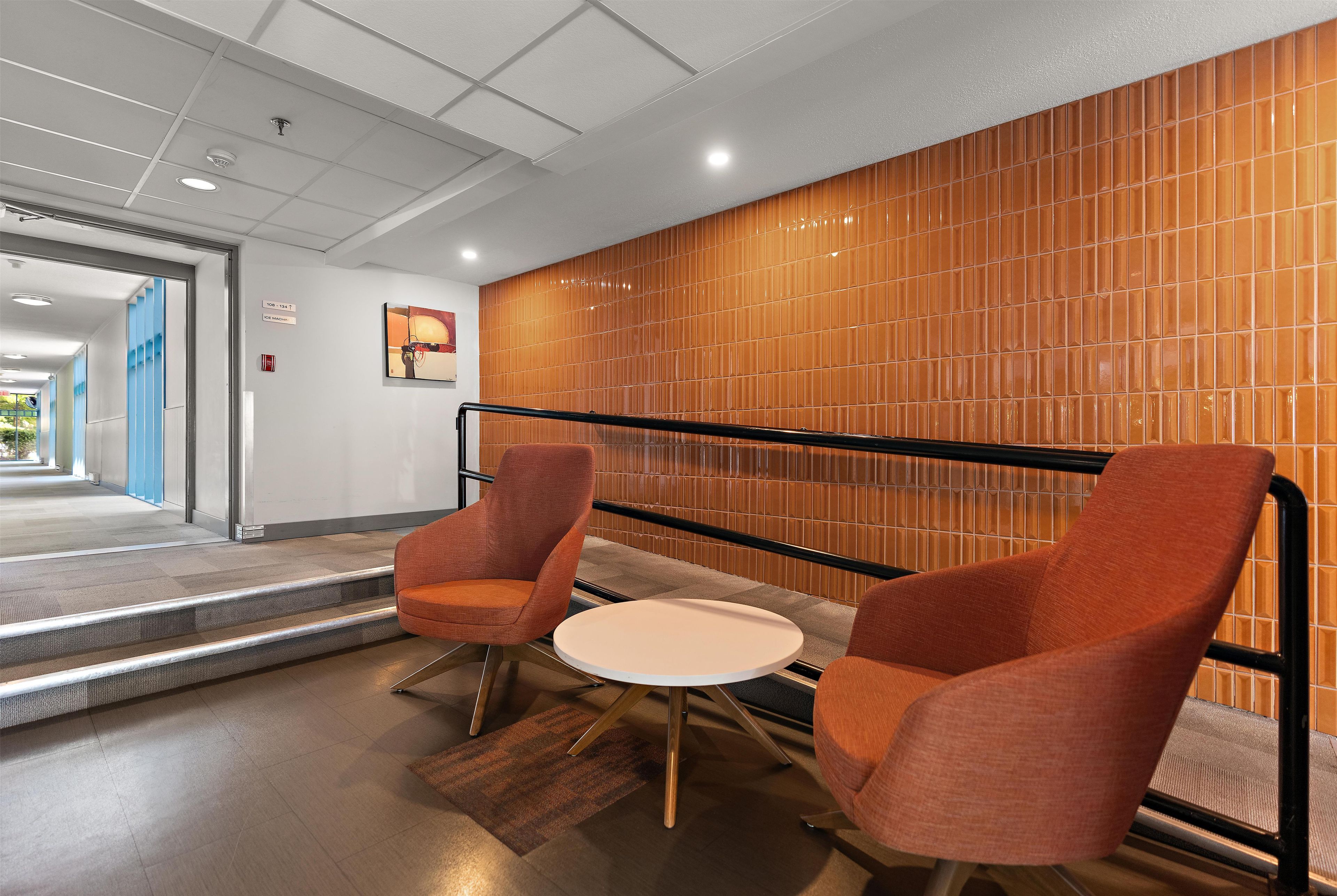 Un interior moderno con dos sillas naranjas, una mesita redonda y una pared de madera con diseño de cuadrícula.