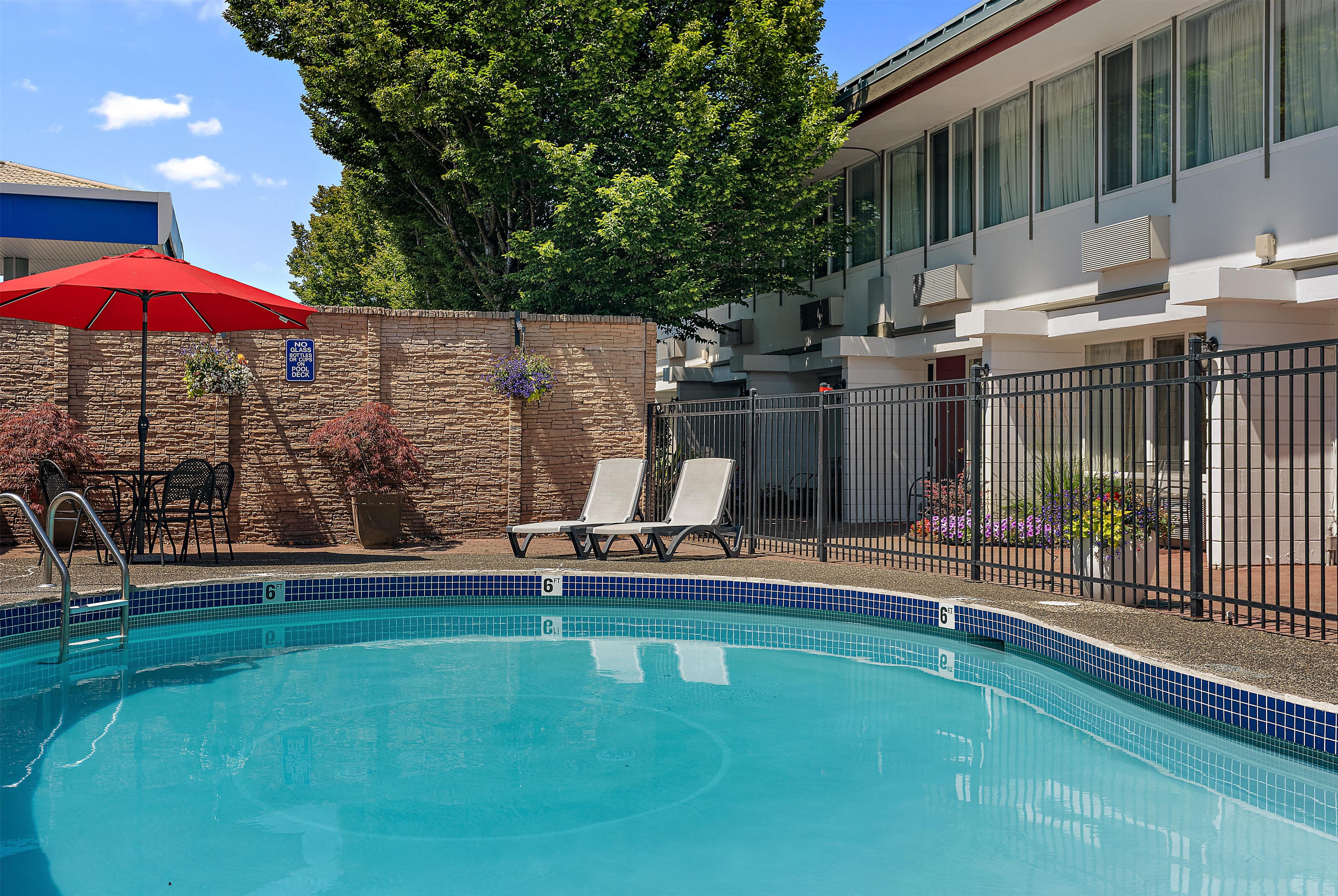 A swimming pool with a 6 ft depth marker, surrounded by a stone wall, with a red umbrella and lounge chairs.