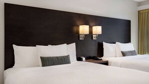 Een hotelkamer met twee bedden, een donker hoofdeinde, wandlampen en een telefoon op het nachtkastje.