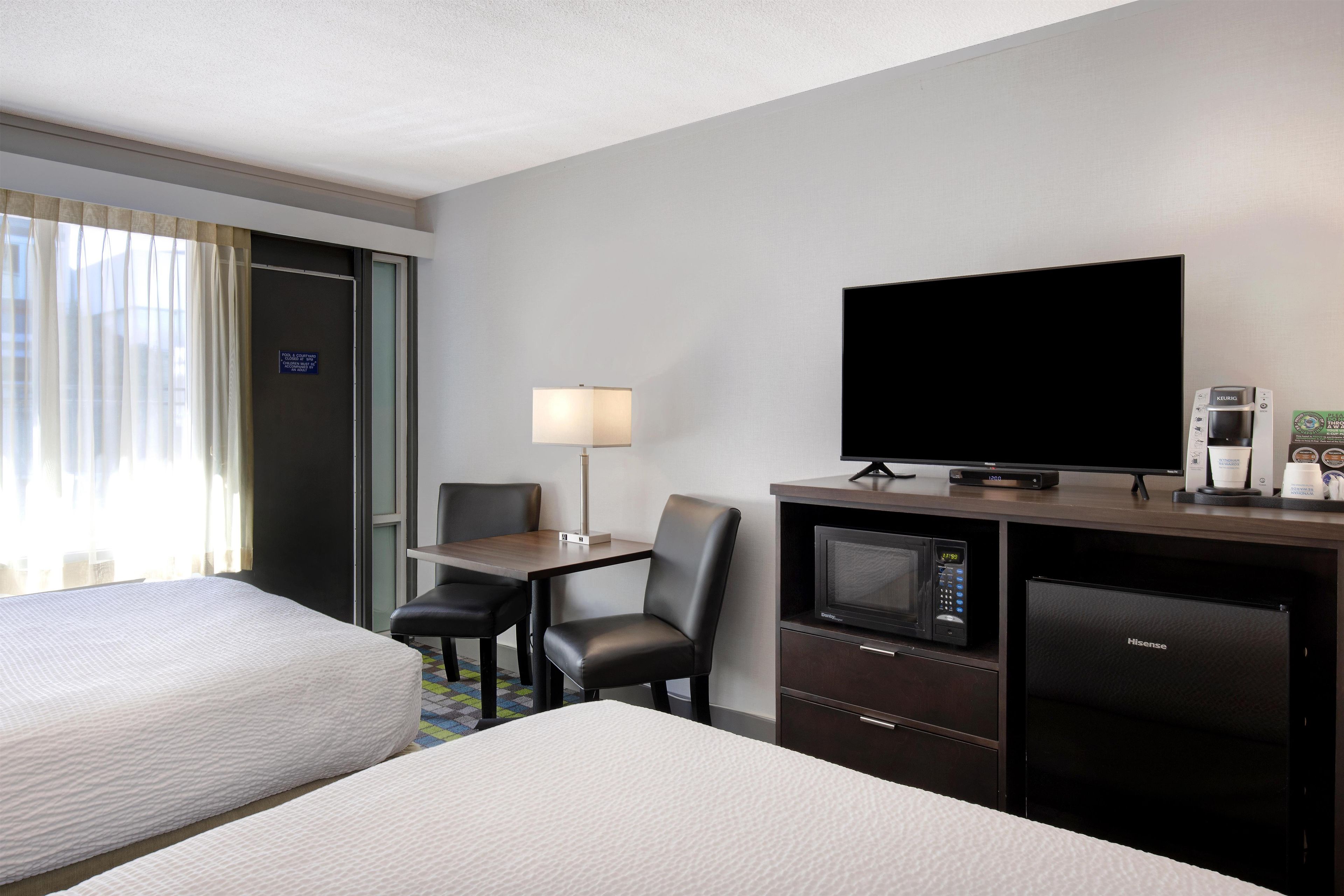 A hotel room with two beds, a desk with a television, a microwave, and a coffee maker.