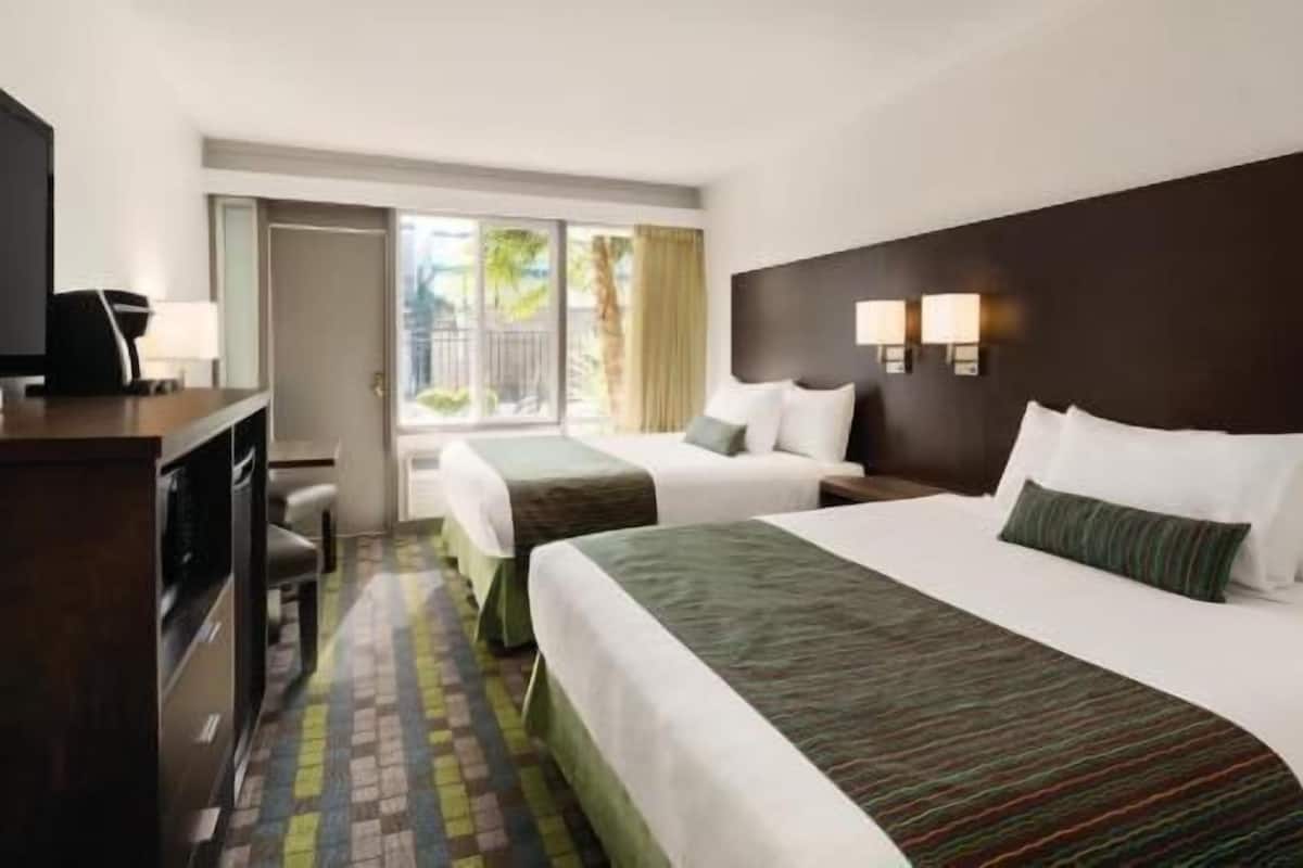 Ein Hotelzimmer mit zwei Betten, einem Schreibtisch mit Stuhl, einem Fernseher und einem Fenster mit Vorhängen.