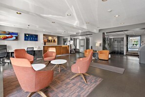 Un vestíbulo de hotel moderno con áreas de descanso, una recepción y un televisor mostrando el pronóstico del tiempo.