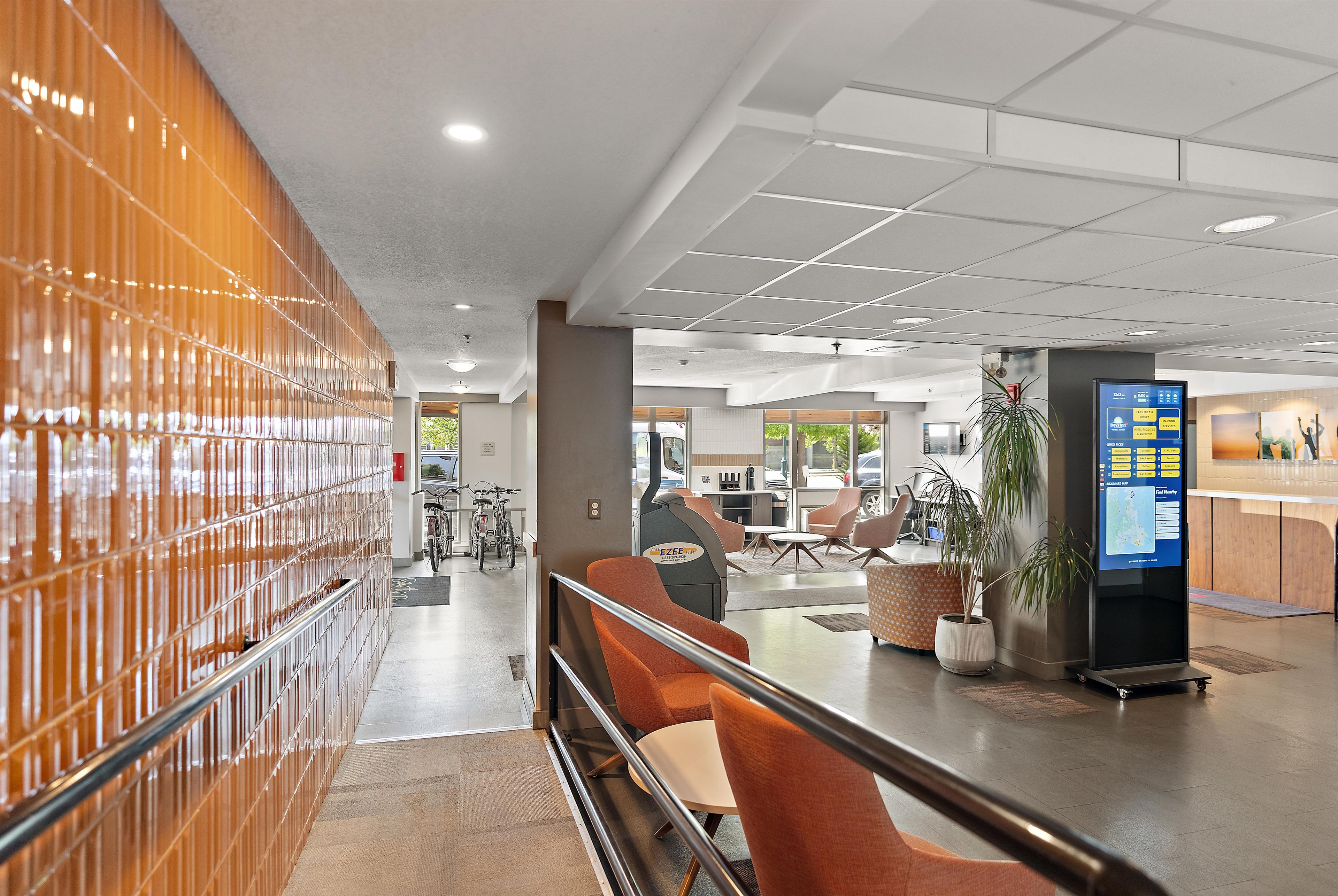 A modern hotel lobby with a seating area, a reception desk, and a digital information kiosk.